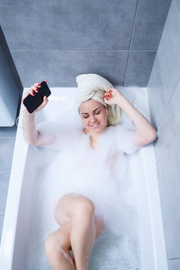 Evde banyo yaparken müzik dinleyen ve şarkı söyleyen güzel bir genç kadın. Zor bir günün ardından rahatla. Spa gevşetici işlem.