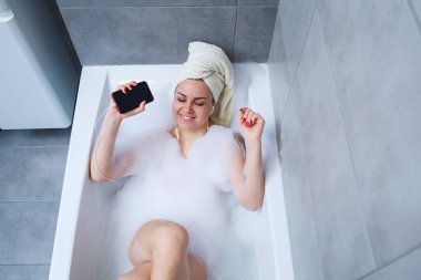 Evde banyo yaparken müzik dinleyen ve şarkı söyleyen güzel bir genç kadın. Zor bir günün ardından rahatla. Spa gevşetici işlem.