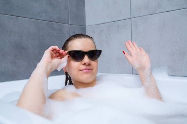 Güneş gözlüklü genç bir kadın bir güzellik salonunda, iç mekanda spa tedavisi görüyor. Tuvalette keten giymeden rahatla. Vücut bakımı ve rahatlama kavramı.