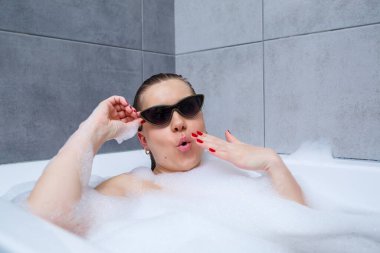 Güneş gözlüklü genç bir kadın bir güzellik salonunda, iç mekanda spa tedavisi görüyor. Tuvalette keten giymeden rahatla. Vücut bakımı ve rahatlama kavramı.