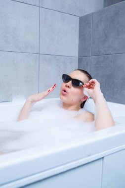 Güneş gözlüklü genç bir kadın bir güzellik salonunda, iç mekanda spa tedavisi görüyor. Tuvalette keten giymeden rahatla. Vücut bakımı ve rahatlama kavramı.
