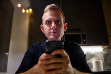 Genç iş adamı evde çalışıyor, mutfak masasında dizüstü bilgisayarla oturuyor, cep telefonuna bakıyor. Başarılı bir girişimci modern evinde bağımsız olarak oturur ve çalışır..