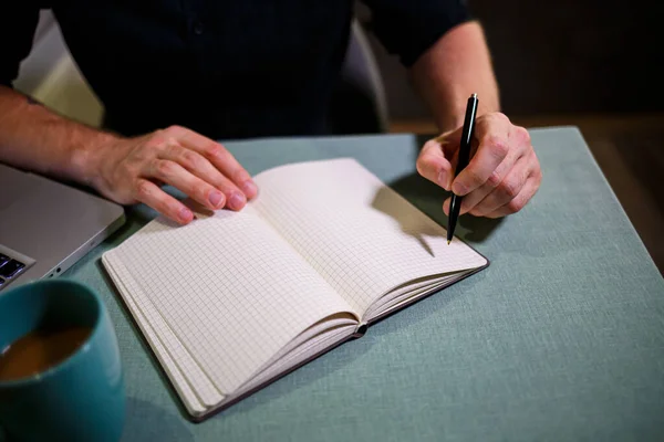 A man makes a record with a pen in a notebook. A book for recording important matters. Diary of a businessman