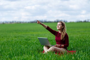 Genç başarılı kadın elinde dizüstü bilgisayarla yeşil çimlerin üzerinde oturuyor. Doğa üzerinde çalış. Gözlerden uzak bir yerde çalışan öğrenci kız. Yeni iş fikirleri