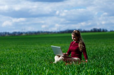 Kucağında dizüstü bilgisayarla çimenlerin üzerinde neşeli genç bir kız. O, ellerini kaldırdı ve güldü. Klasik bir öğrencinin yaşam tarzında mutluluk. Doğa üzerinde çalış. İyi bir iş gününden sonra dinlen..