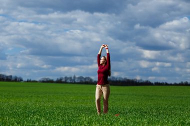 Güzel sarışın kadın parkta yeşil çimlerin üzerinde duruyor. Bulutlu mavi gökyüzü. Kız gülümsüyor ve güzel bir günün tadını çıkarıyor..