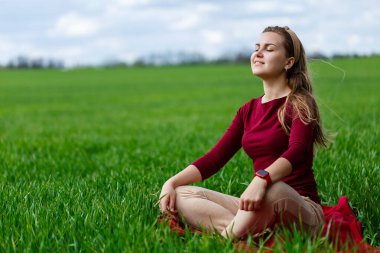 Güzel bir kadın çimlerin üzerinde oturuyor ve dinleniyor. Kız gözlerini kapattı ve güneşin tadını çıkardı. Gülümsüyor ve sıcak bir günün tadını çıkarıyor..