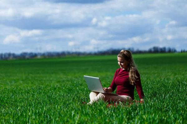 Kucağında dizüstü bilgisayarla çimenlerin üzerinde neşeli genç bir kız. O, ellerini kaldırdı ve güldü. Klasik bir öğrencinin yaşam tarzında mutluluk. Doğa üzerinde çalış. İyi bir iş gününden sonra dinlen..