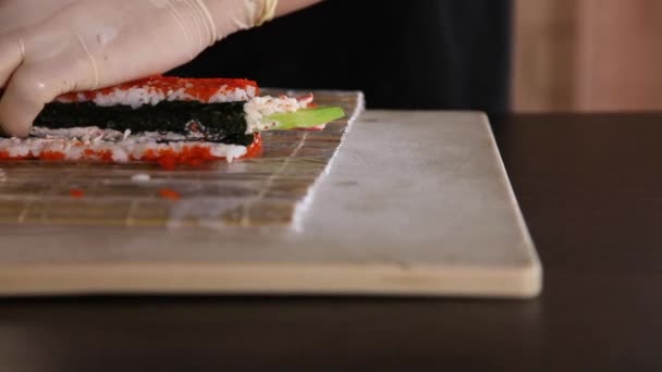 Närbild av Sushi tillverkningsprocessen.Rullar sushi roll.Rice, nori, avokado, krabba, röd tobiko kaviar.Kockar händer.Bambu matta — Stockvideo