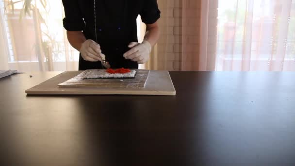Chef de sushi masculino pone tobiko de caviar rojo en un arroz y nori.Sushi proceso de fabricación — Vídeo de stock