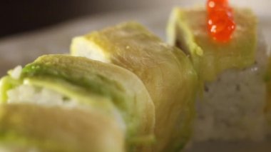Kırmızı havyarla süsleme işlemi. Avokado dilimleriyle süslenmiş suşi dürümleri. Makro.