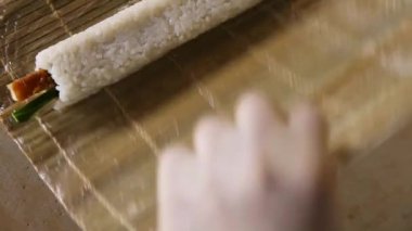 Şefin ellerinin suşi rulosunu bambu matına sarması. Suşi hazırlıyor. Suşi rulosunu yuvarlıyor. Yukarıdan görünüyor.