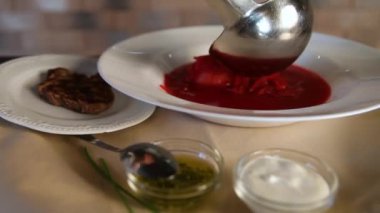 Ekşi krema ve kızarmış etin yanında borç çorbası. Geleneksel Rus borsch çorbasını temiz beyaz bir tabağa dökme süreci..
