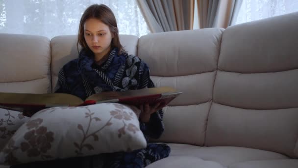 Menina adolescente lendo um livro vermelho gigante quarentena em casa durante a pandemia COVID-19. — Vídeo de Stock