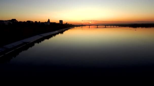 Ciemny widok z lotu ptaka na most przez szeroką rzekę o zachodzie słońca.Zachód słońca odbija się w wody.Kopiuj space.4k. — Wideo stockowe
