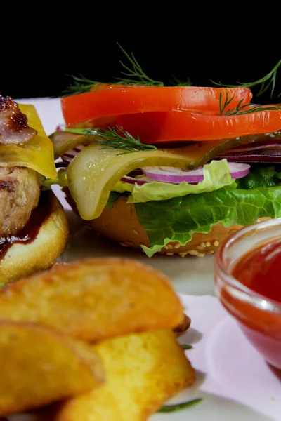 Kızarmış domuz pastırmalı hamburger, patates kızartması, sebze ve ketçaplı beyaz bir tabakta. Yakın plan..