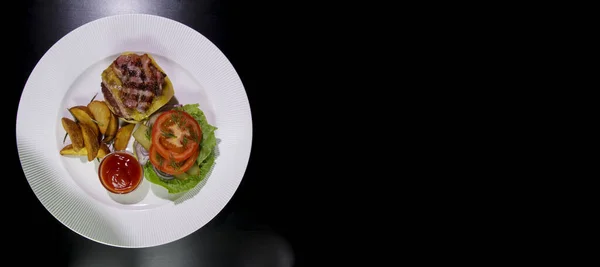 Kızarmış domuz pastırmalı hamburger, patates kızartması, sebze ve ketçap beyaz tabakta. Siyah bir arkaplanda izole edilmiş. Yukarıdan görüş. Yatay bileşim. Sağlıksız yemek..