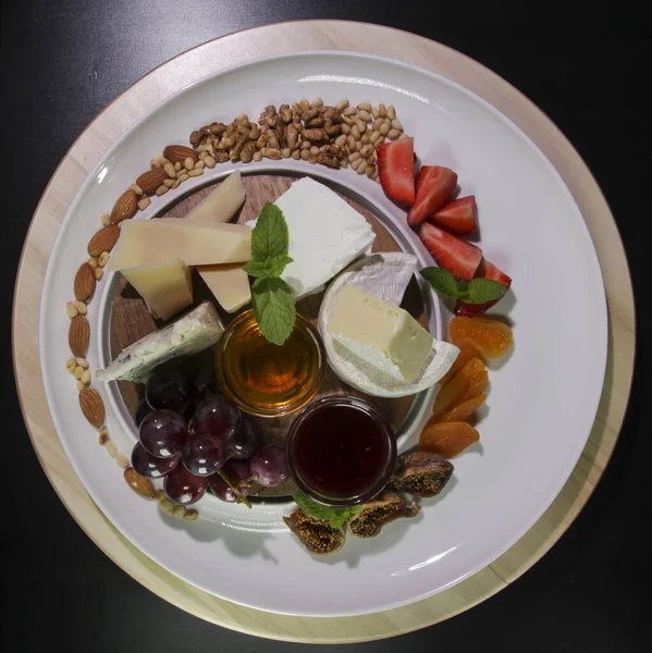 Peynir tabağı. Siyah bir arka planda izole edilmiş. Camembert peyniri, parmesan peyniri, üzümle servis edilen mavi peynir, reçel, incir, bal, çilek, kurutulmuş kayısı ve fındık..
