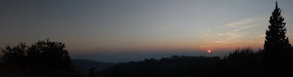 Gece yarısı panoramik gün batımı manzarası. Kırmızı güneş, ağaç siluetleri, ufuk çizgisi