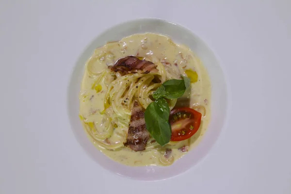 Carbonara soslu makarna, vişneli domates, ızgara domuz pastırması, peynir, beyaz tabakta nane. Yakından bak..
