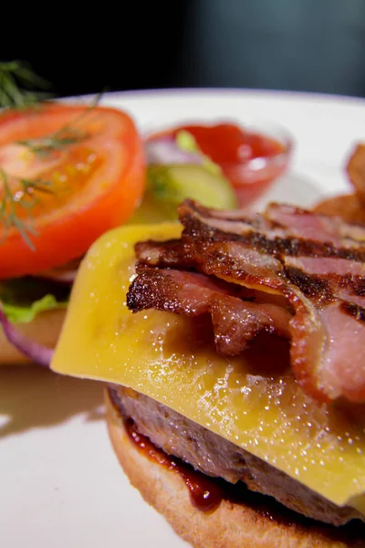 Kızarmış pastırmalı hamburger, patates kızartması, sebze ve ketçaplı beyaz tabakta. Enerji yoğunluğunda yiyecek..