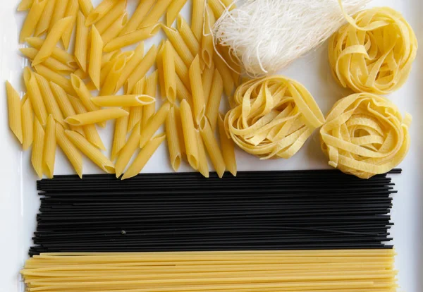 Çeşitli kuru makarna çeşitlerini kapatın. Penne, spagetti, erişte, siyah spagetti, fettucine, funchoz..