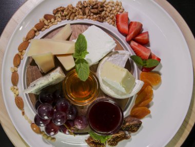 Peynir tabağı. Camembert peyniri, parmesan peyniri, üzümlü mavi peynir, reçel, incir, bal, çilek, kurutulmuş kayısı ve fındıklı beyaz tabakta. Yukarıdan görüş..