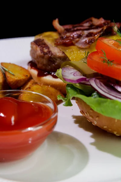 Kızarmış pastırmalı hamburger, patates kızartması, sebze ve ketçaplı beyaz tabakta. Yakından. Kalori alımı..