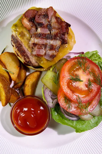 Kızarmış domuz pastırmalı hamburger, patates kızartması, sebze ve ketçaplı beyaz bir tabakta. Yukarıdan bak. Yakın plan. Kalori alımı..