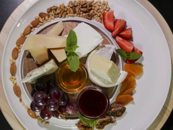 Peynir tabağı. Camembert peyniri, parmesan peyniri, üzümlü mavi peynir, reçel, incir, bal, çilek, kurutulmuş kayısı ve fındıklı beyaz tabakta. Yukarıdan görüş..