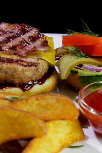 Sağlıksız yiyecek. Kızarmış pastırmalı hamburger, patates kızartması, sebze ve ketçap. Yakın plan..