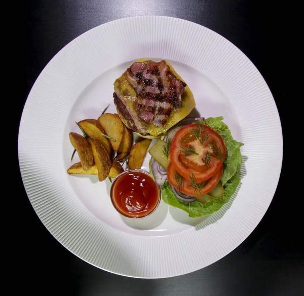 Kızarmış domuz pastırmalı hamburger, patates kızartması, sebze ve ketçap beyaz bir tabakta. Siyah bir arka planda izole edilmiş. Yukarıdan görüş..