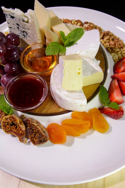 Peynir tabağı. Camembert peyniri, parmesan peyniri, üzümlü mavi peynir, reçel, incir, bal, çilek, kurutulmuş kayısı ve fındıklı beyaz tabak.