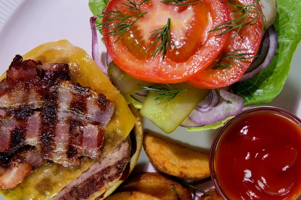 Kızarmış domuz pastırmalı hamburger, patates kızartması, sebze ve ketçaplı beyaz bir tabakta. Yukarıdan bak. Yakın çekim..