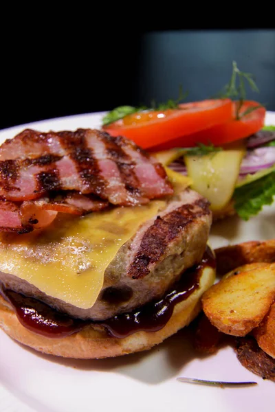 Kızarmış pastırmalı burger, patates kızartması, sebze ve ketçaplı beyaz tabakta. Sağlıksız yemek..