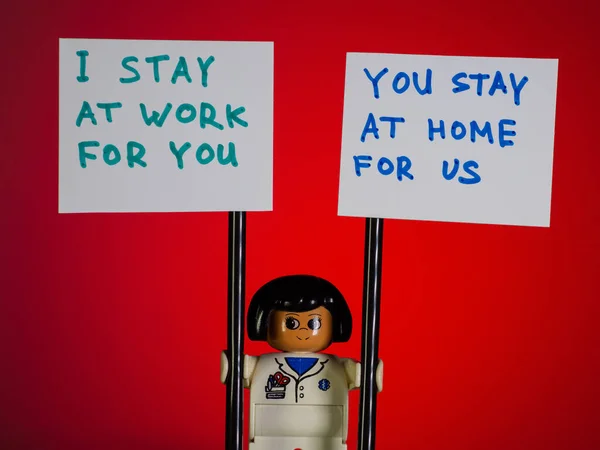 Lego Tıp Doktoru 'nun elinde senin için çalıştığım posterler var, sen de evde kal. COVID-19 karantinada kal. Kırmızı arka plan..