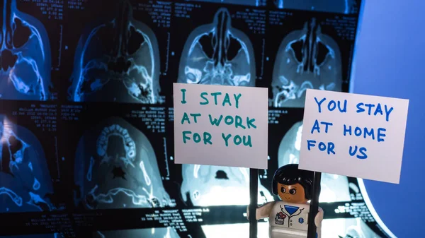 Lego medical doctor holding posters I STAY AT WORK FOR YOU, YOU STAY AT HOME FOR US against the background of CT scan.COVID-19 quarantine staying at home concept.Close-up.