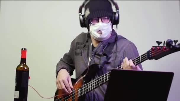 Man i medicinsk mask dricker vin och spelar bas. — Stockvideo