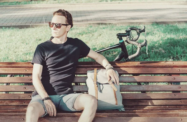 Mężczyzną rowerzysta opiera się na ławeczce, drewniane. — Zdjęcie stockowe