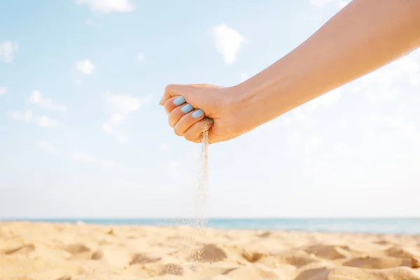 Woman’s hand pours sand outdoor.