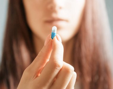 Elinde mavi beyaz kapsül tutan bir kadın..