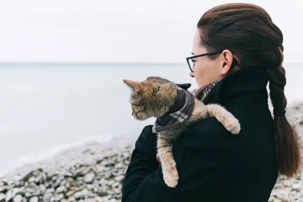 海のそばの海岸に立つバンダナに猫を持つ女性. — ストック写真
