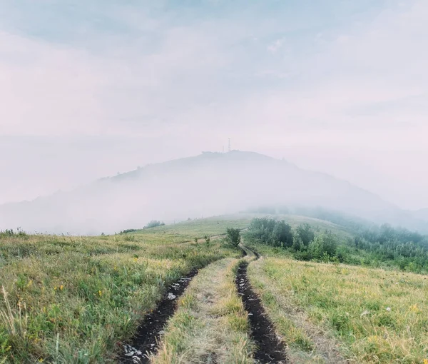 Strada sterrata di fronte alla montagna coperta dalla nebbia . — Foto Stock