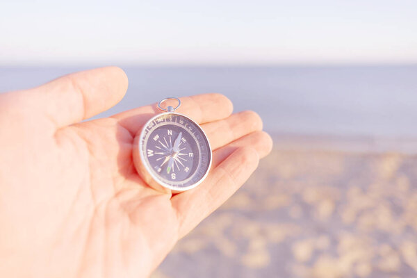 Male hand holding magnetic compass on background of sea coastline, point of view in first person.
