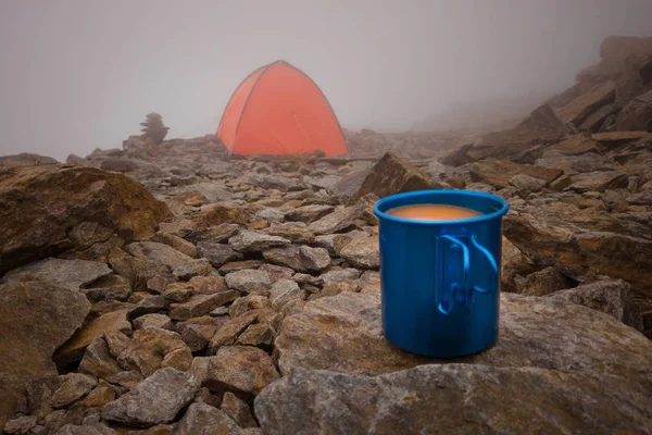 coffee in the mountains in the background tents in the fog. travel mug on the stone. blue cup.