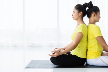Sarı elbiseyle yoga yapan iki genç Asyalı kadın.