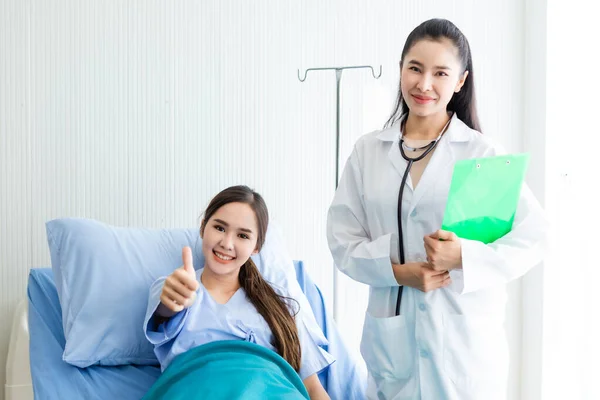 Asiatisk ung kvinnlig patient på sängen visar tummen upp med smiley — Stockfoto