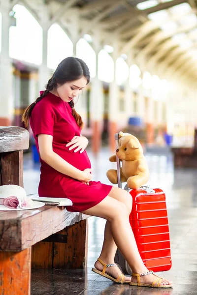 Asiático mulher grávida vestido vermelho sentado em um banco em transportar re — Fotografia de Stock