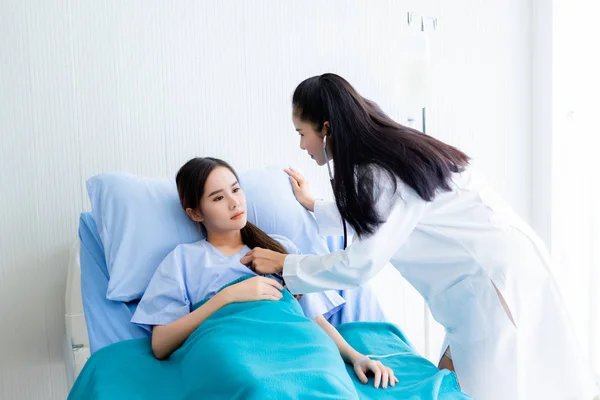 Asiática jovem paciente na cama enquanto médico mãos de verificação — Fotografia de Stock