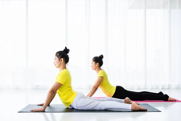 Two young Asian women workout practicing yoga in yellow dress or